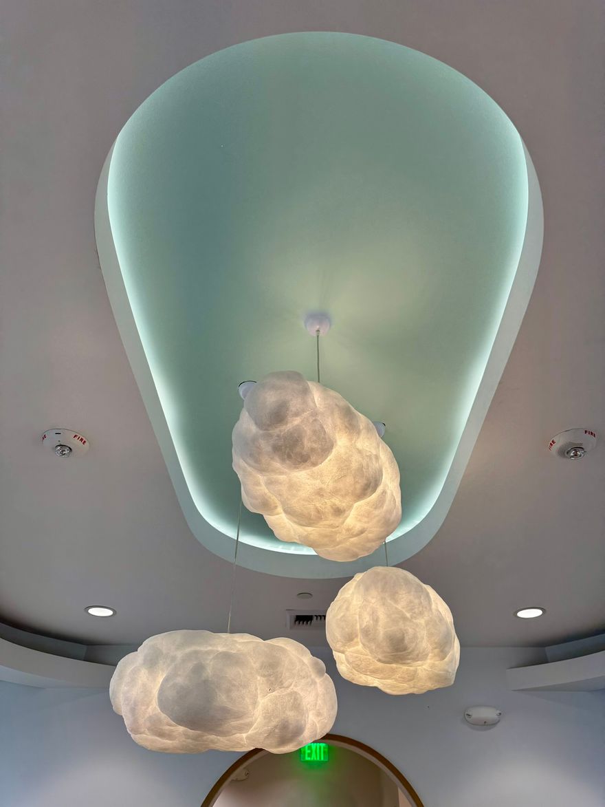 Cloud-shaped pendant lights under a cove-lit ceiling, a Sound Electric commercial lighting install